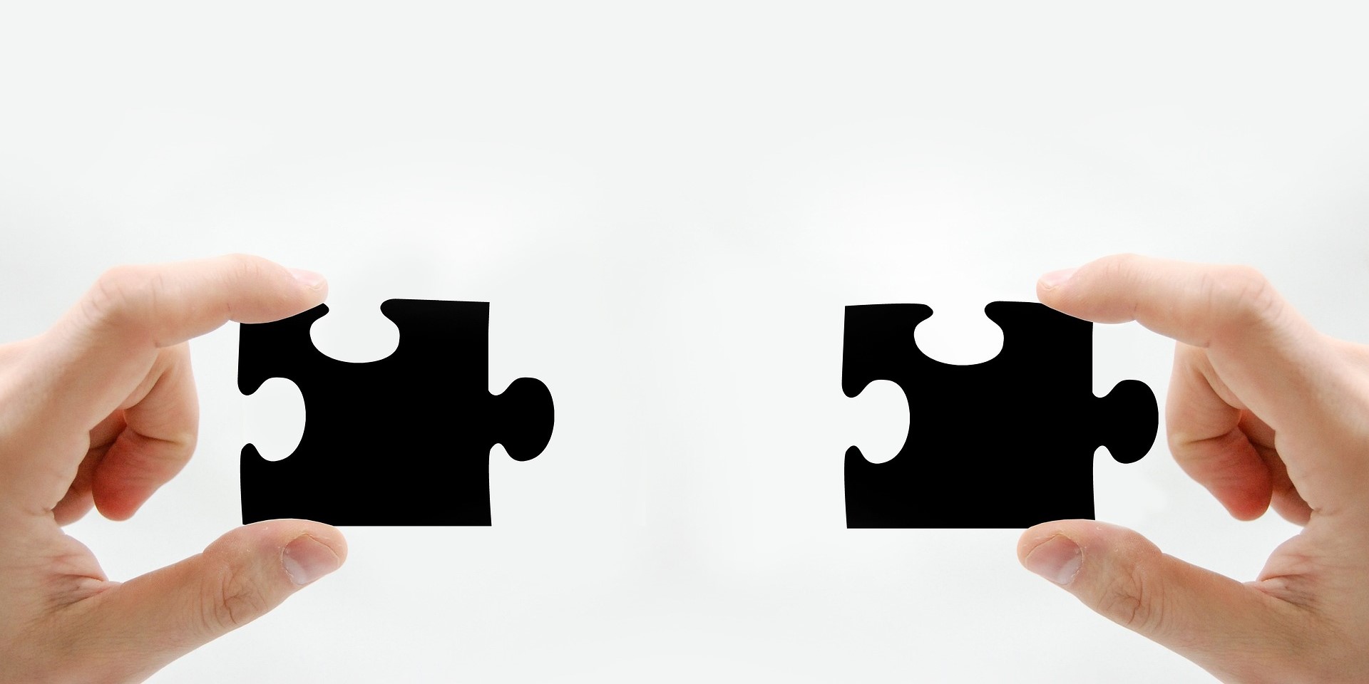 Zwei Puzzleteile die von zwei Händen gehalten werden und ineinanderpassen.