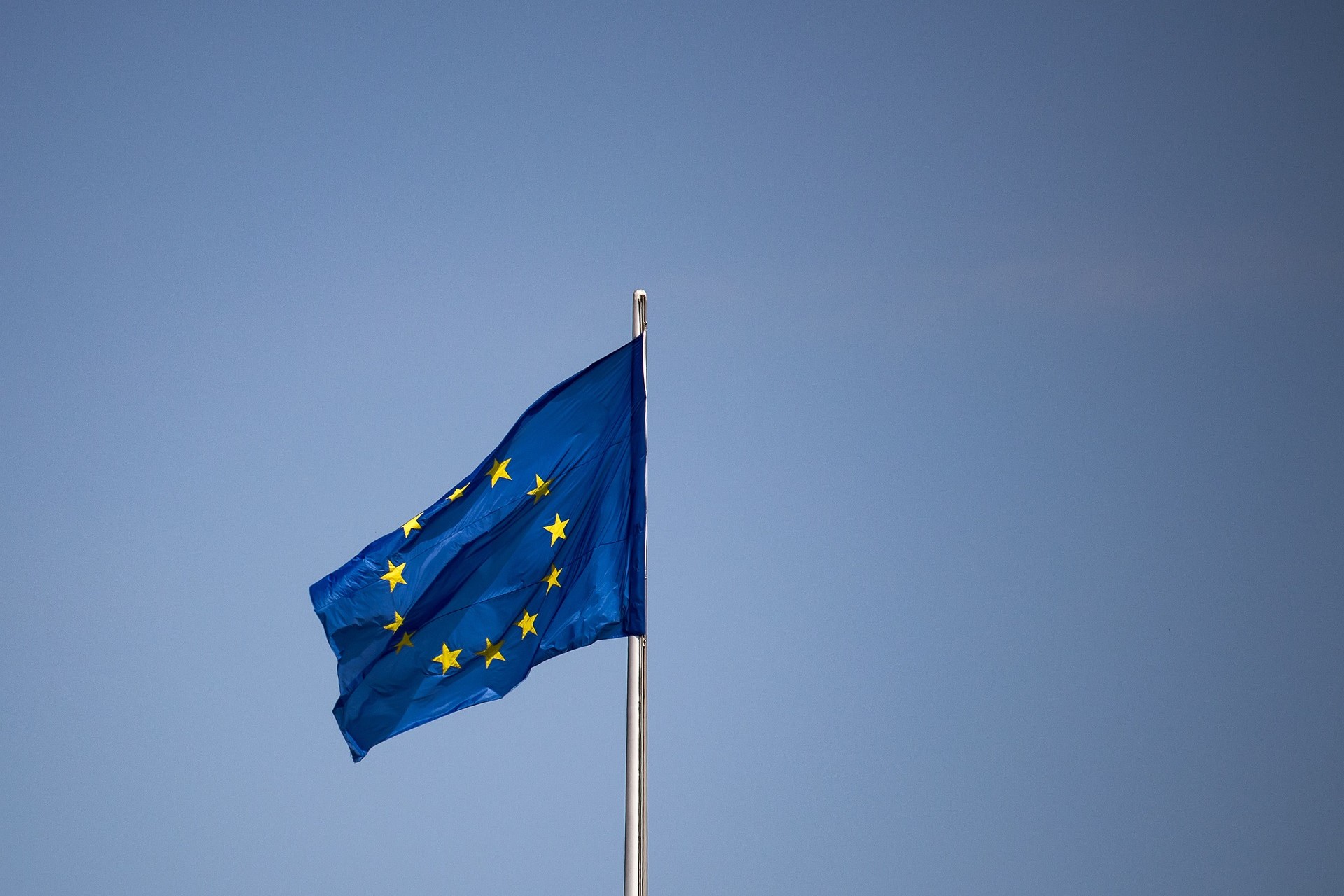 Die Europafahne (Kreis aus zwölf goldenen Sternen auf blauem Hintergrund) flattert im Wind. Im Hintergrund ist nur der blaue Himmel zu sehen.