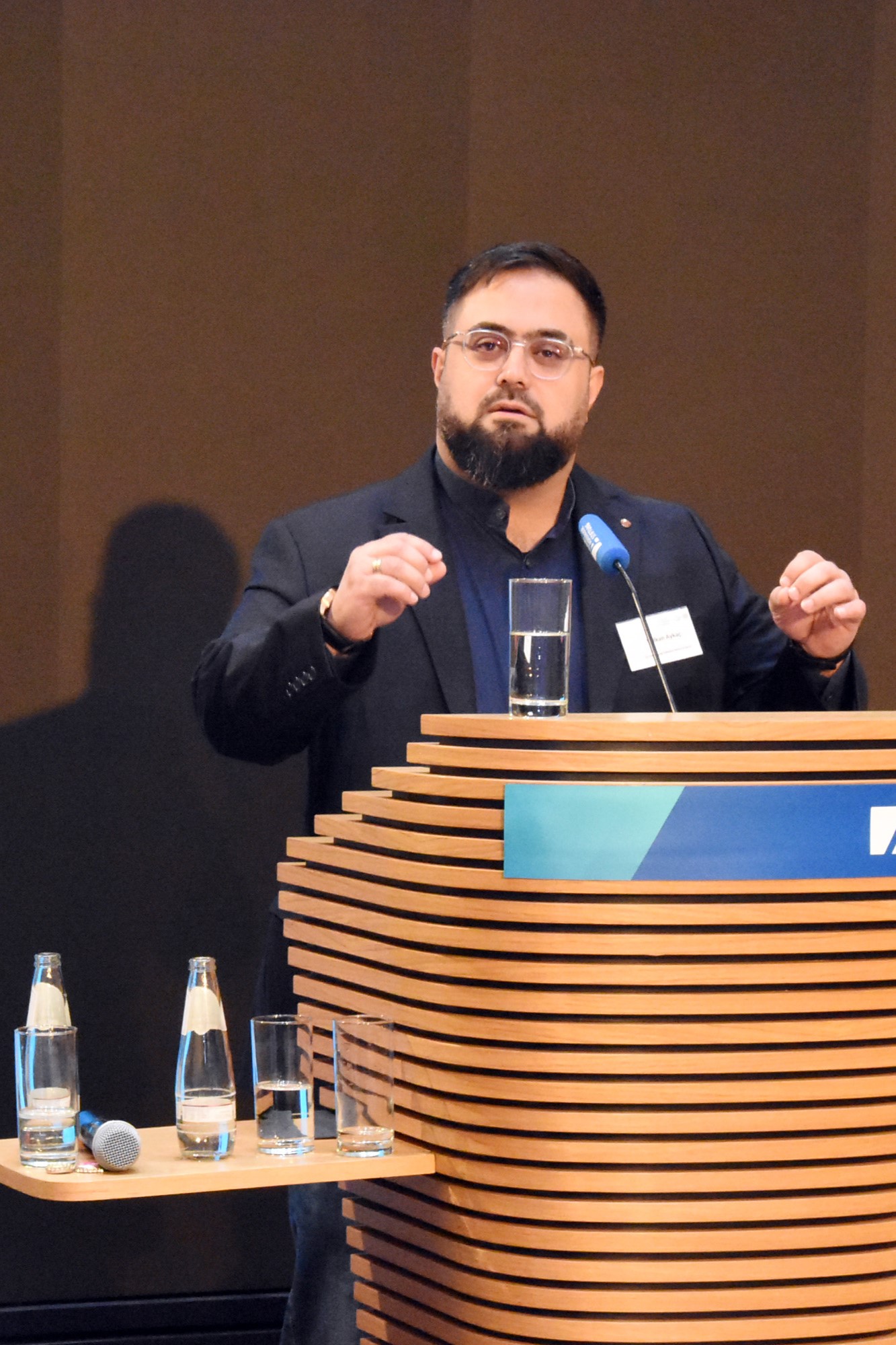 Ein Mann mittleren Alters, mit Anzug und Brille hält eine Rede auf einer Konferenz.