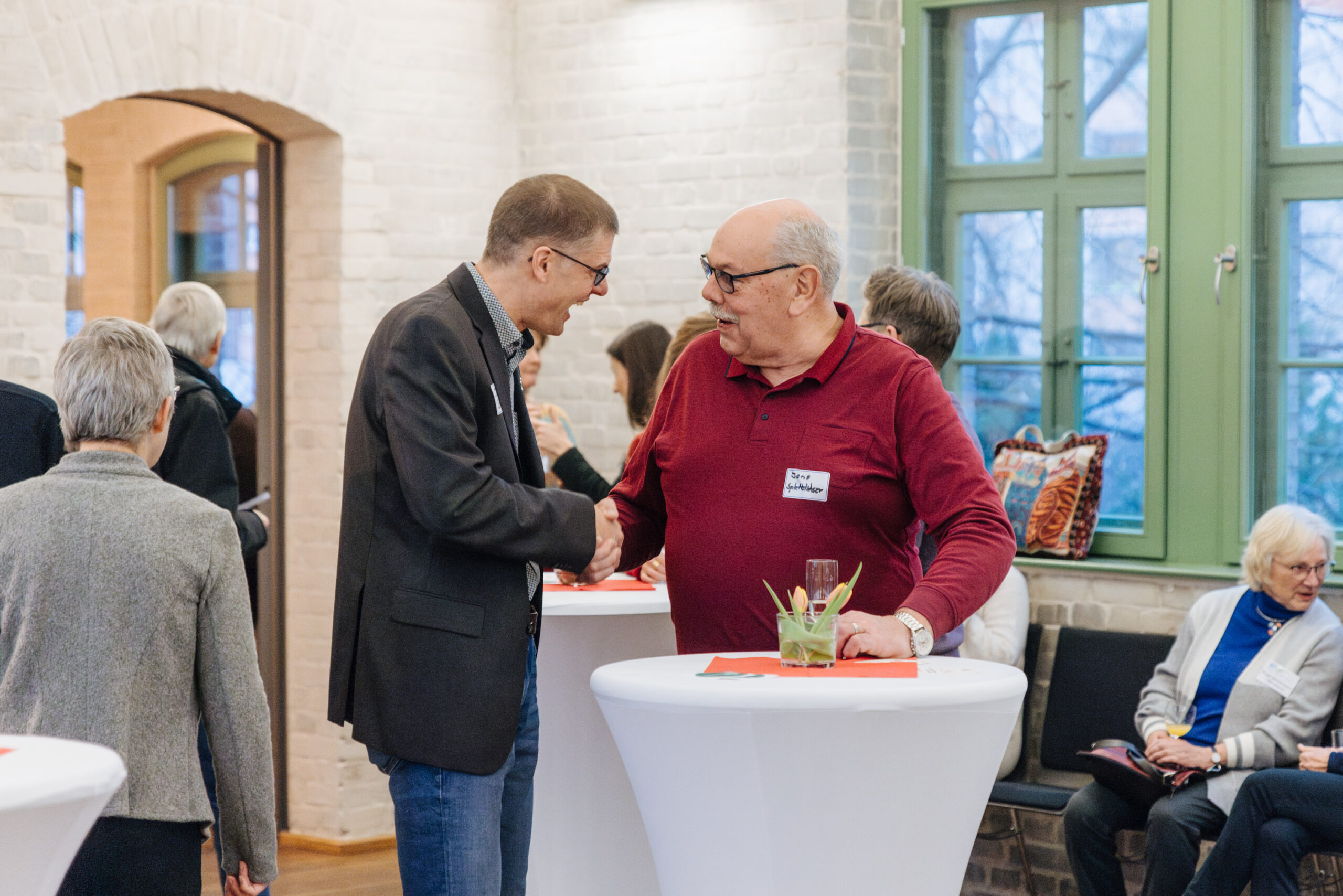 Zwei Männer begrüßen sich am Rand einer Veranstaltung herzlich mit einem Handschlag.